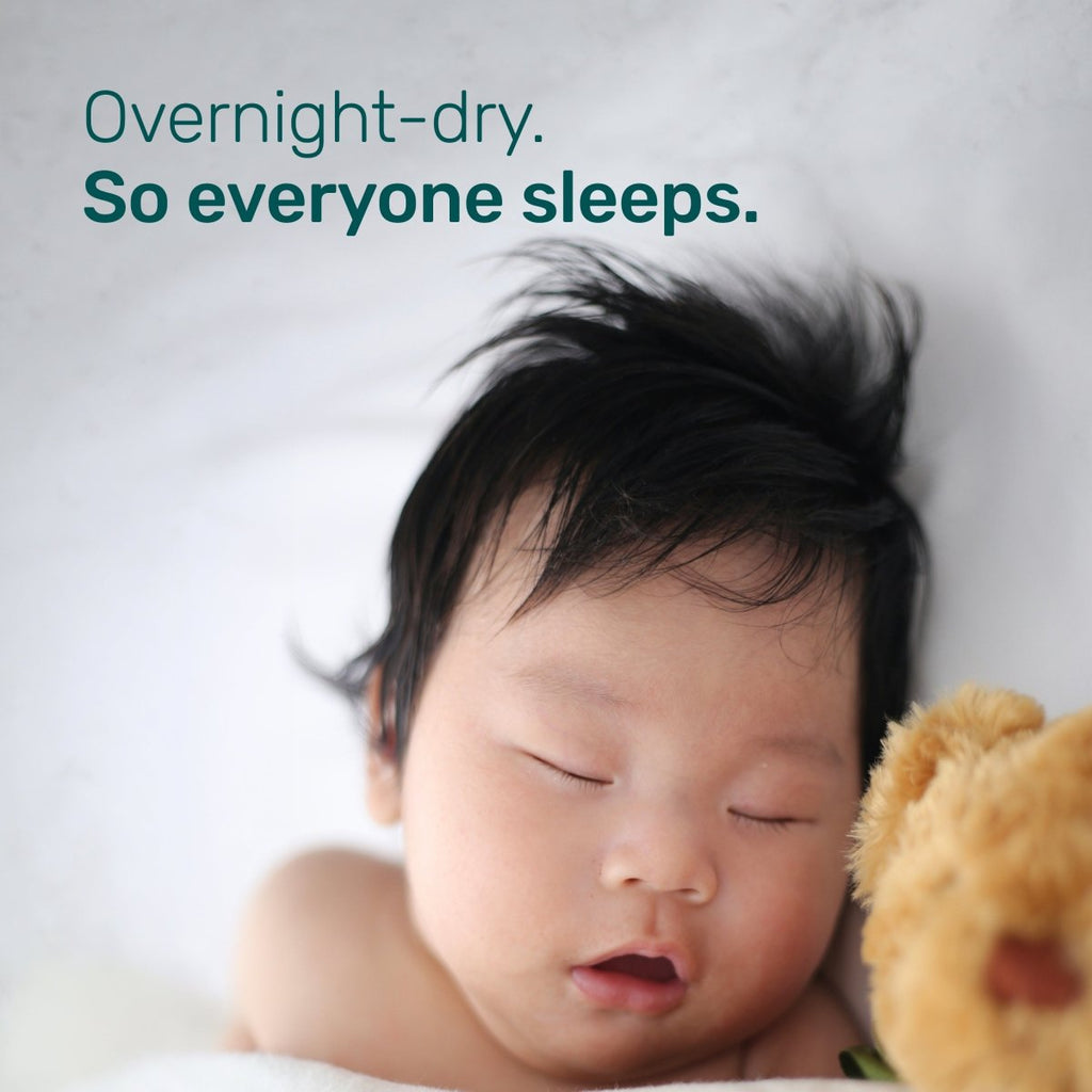 Sleeping baby with dark hair next to a teddy bear, with the text “Overnight-dry. So everyone sleeps.”